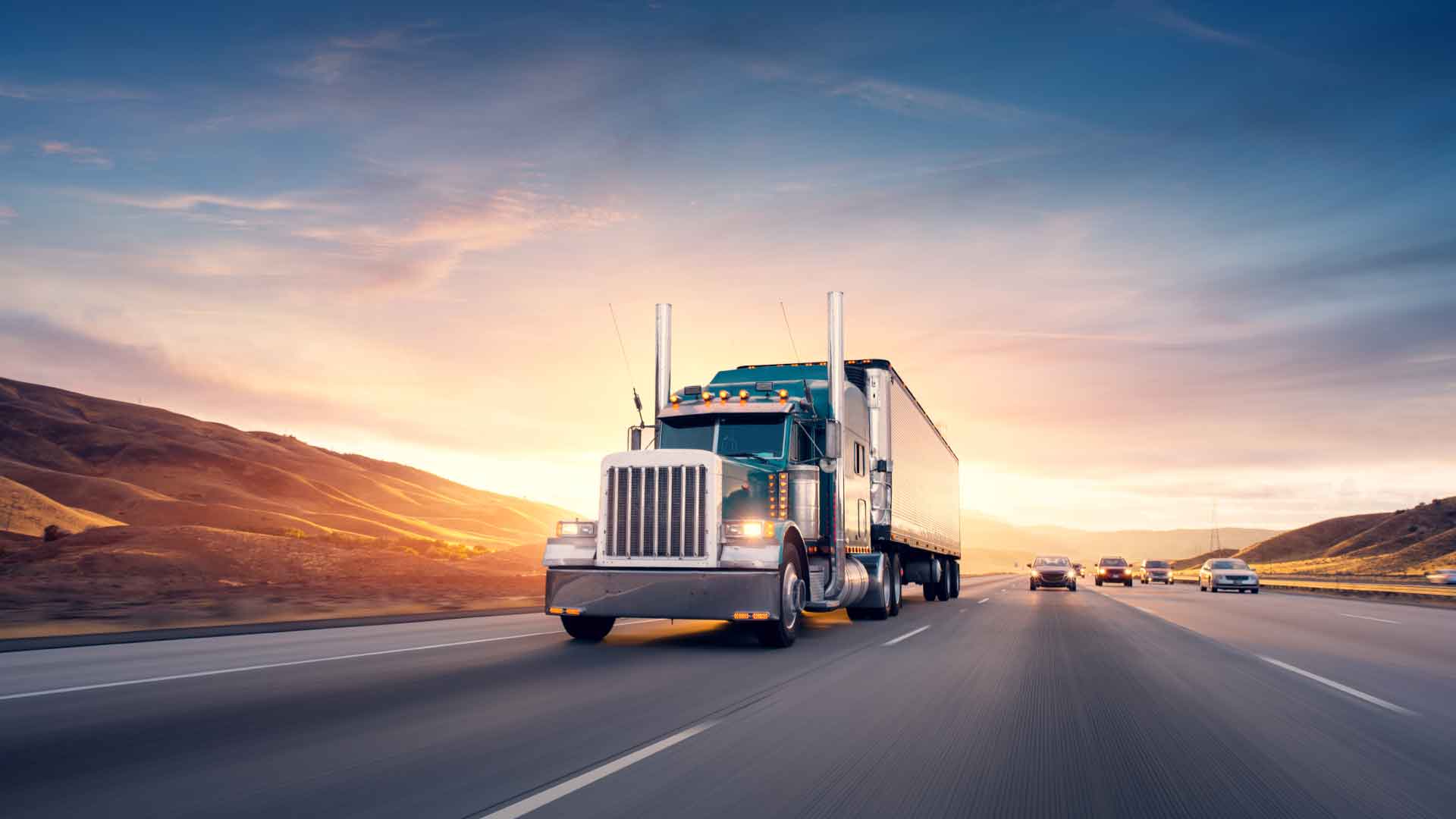 Regional A semi tractor and dry van trailer driving away from a beautiful sunset down the highway, surrounded by cars.