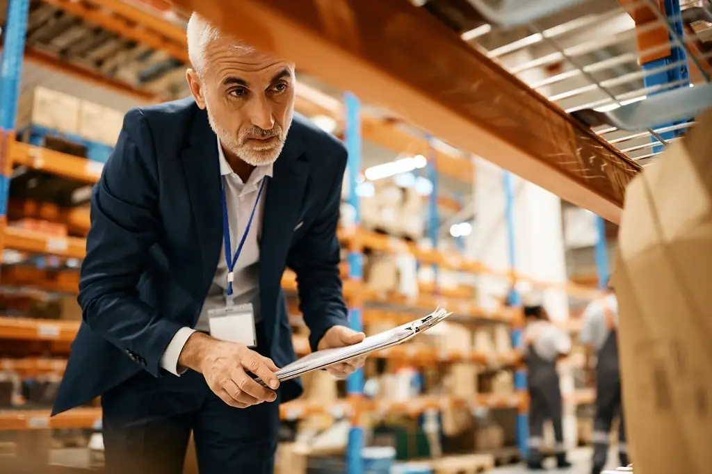mature warehouse manager checking stock of packages at storage compartment